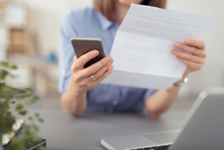 frau schaut auf einen brief und tippt auf ihr mobiltelefon frau schaut auf einen brief und tippt auf ihr mobiltelefon